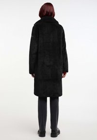 Zwarte nepbontjas met een kraag, rechte silhouet en lange mouwen. Heeft een gladde textuur en een knielange uitstraling.