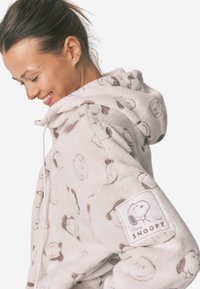 Cremefarvet hoodie lavet af blødt stof, med et Snoopy print og et kvadratisk logo-patch på ærmet. Snor i hætten og struktureret finish.