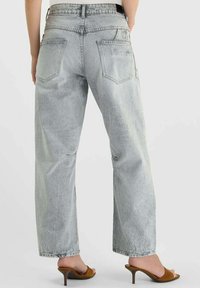 Jean gris clair taille haute à coupe décontractée, avec deux poches arrière et texture délavée, associé à des sandales à talons marron.