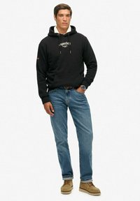 Czarna bawełniana bluza z kapturem, z kieszenią z przodu i sznurkiem, w połączeniu z niebieskimi dżinsami i jasnobrązowym obuwiem sznurowanym. Prosty, codzienny strój.