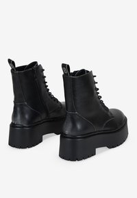 Botas de tobillo de cuero negro con suela gruesa tipo plataforma, con cordones en la parte delantera, cremallera lateral y una lengüeta en la parte posterior.