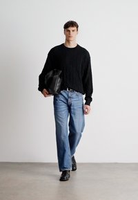 Maglione nero a treccia con vestibilità oversize, jeans dritti blu chiaro e scarpe in pelle nera. Porta una borsa in pelle nera.