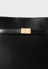 Schwarzer Ledergürtel mit schmalem Riemen und rechteckiger Schnalle aus goldfarbenem Metall, vor weißem Hintergrund dargestellt.