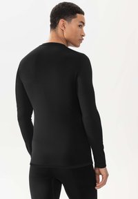 Chemise noire à manches longues en matière lisse et extensible, avec un col rond et une coupe ajustée. Idéale pour être portée en superposition.