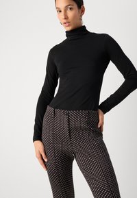 Haut noir à col roulé à manches longues associé à un pantalon noir à motifs présentant un design de cœurs légers, avec une coupe structurée et des poches avant.