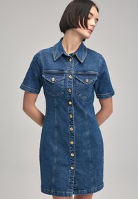 Robe en denim à manches courtes, col, boutons pression dorés, deux poches poitrine et coupe ajustée. Couleur bleue avec une texture denim classique.