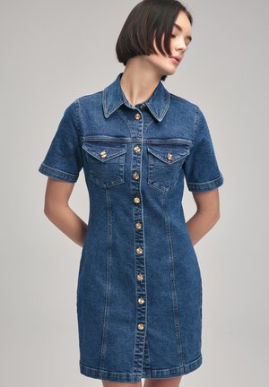 Robe en denim à manches courtes, col, boutons pression dorés, deux poches poitrine et coupe ajustée. Couleur bleue avec une texture denim classique.