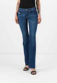 Jean flare en denim bleu foncé avec une taille mi-haute, présentant des poches avant et un subtil détail de couture. Texture lisse, coupe classique.