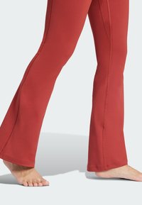 Pantalons de sport évasés en tissu brun rouge riche. Caractérisés par des coutures sans couture et une texture lisse, avec une taille ajustée et une jambe décontractée.