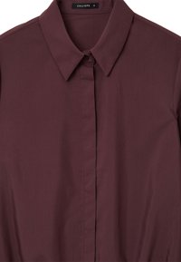 Camicia button-up color bordeaux con colletto classico, realizzata in tessuto liscio, con patta frontale e un'etichetta con la scritta "CALLIOPE". Taglia S.