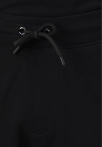 Jogging noir avec taille à cordon, présentant une texture de tissu lisse et des détails de couture subtils. Design minimaliste sans motifs visibles.