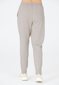 Lichtgrijze joggers met een elastische tailleband en zijzakken, met een gladde textuur en taps toelopende pijpen, gecombineerd met witte sneakers.