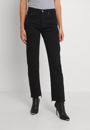 Vrouw draagt zwarte rechte jeans met hoge taille en rafelige zomen en zwarte puntige enkellaarzen met hoge hakken en gouden tips.