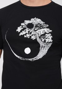 Black t-shirt featuring a white graphic design of a tree integrated with a yin-yang symbol, highlighting detailed branches and leaves.