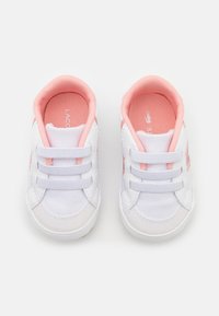 Weiße Leinenschuhe mit pinken Akzenten, abgerundetem Zehenbereich, drei vorderen Riemen und einer strukturierten Innensohle. Die Sohle ist leicht und gummiartig.