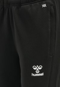 Schwarze Sporthosen mit elastischem Bund, ausgestattet mit einem weißen Logo auf dem linken Oberschenkel und einem glatten, strukturierten Stoff.