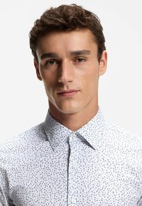 Weißes Hemd mit Knopfleiste und blauem Blattmuster, ausgestattet mit einem klassischen Kragen und glatter Stofftextur. Saubere Nähte und Plastikknöpfe.