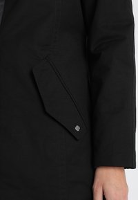 Czarny płaszcz o gładkiej fakturze, z ukośną kieszenią boczną z metalowym akcentem oraz dopasowanym krojem w okolicy rękawów.