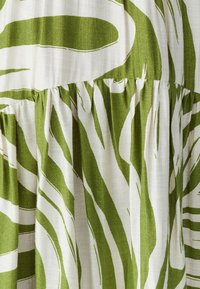 Robe verte et blanche avec un motif de rayures zèbre, fabriquée dans un tissu texturé et présentant des détails froncés à la taille.