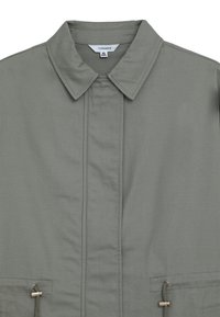Giacca verde oliva con colletto a camicia, zip frontale, due tasche laterali e dettagli metallici sui laccetti.