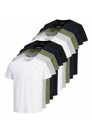 Junger Mann steht, trägt ein olivgrünes kurzärmeliges T-Shirt und blaue Jeans, mit einer Hand in der Tasche und neutralem Hintergrund.