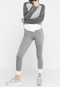 Sweatshirt à capuche gris à manches longues avec des accents blancs, superposé sur une chemise blanche ; leggings gris avec des rayures blanches ; chaussures de sport grises.