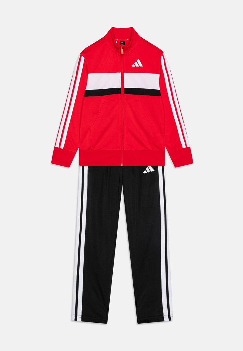 Röd zip-up träningsjacka med vita och svarta horisontella ränder, tillsammans med svarta byxor med vita sidostråkar. Tillverkad av slät tyg.