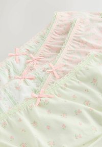 Trois paires de slips pour femmes à motifs floraux pastel, ornés de nœuds roses et de bordures en dentelle, disposés en chevauchement sur une surface claire.