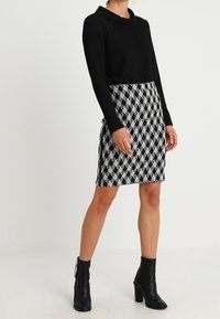 Top negro de manga larga combinado con una falda corta de cuadros en blanco y negro, con cuello de cisne, y acompañado de botas negras hasta el tobillo.