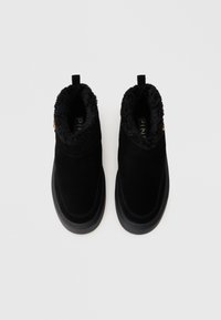 Botas de tornozelo em camurça preta com um forro de pelúcia preta em pele sintética e sola de borracha texturizada. Inclui uma aba para facilitar o calçar.