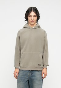 Grå hettegenser laget av mykt stoff, med en frontlomme, justerbar hette og ribbestrikkede mansjetter. Løs passform, minimalistisk design med diskret branding.