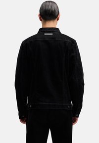 Czarna kurtka dżinsowa o klasycznym kroju, z widocznym przeszyciem, mankietami zapinanymi na guziki oraz małą metką na górnej części pleców. Tkanina o wyraźnej fakturze.
