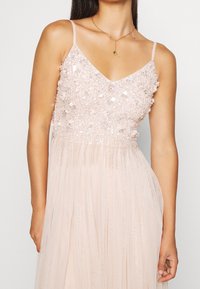 Blush-pink Abendkleid mit einem bestickten, glitzernden Oberteil, dünnen Trägern und einem fließenden, plissierten Rock. Sanfter Schimmer und weiche Textur sind hervorstechend.