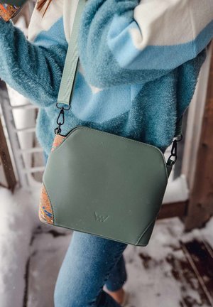 Grüne vegane Leder-Umhängetasche mit abgerundeten Kanten, Kork-Akzent und verstellbarem Riemen. Verfügt über ein dezentes Logo und eine weiche Textur.