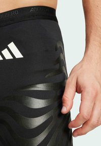 Zwarte sportleggings met een textuur van een donkere zebra-streep patroon en een tailleband met "ADIZERO" branding.