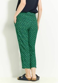 Zelené tištěné kalhoty s motivem listů, elastickým pasem a bočními kapsami, doplněné námořnickými sandály.