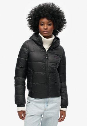 Giubbotto piumino nero con cappuccio, chiusura con zip e polsini elastici. Presenta un logo discreto sul petto e una texture trapuntata.