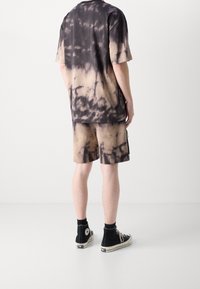 Camisa de manga corta y pantalones cortos de teñido anudado en tonos de marrón y negro, con un ajuste relajado y una textura de algodón suave, combinados con zapatillas negras.