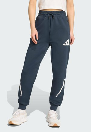 Pantalons de jogging bleu marine avec un cordon de serrage à la taille, rayures blanches en accent et un logo Adidas blanc sur la cuisse gauche. Tissu doux et coupe ajustée.