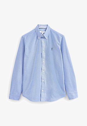 Világoskék, gombos pamut ing, klasszikus gallérral, hosszú ujjakkal, és egy kicsi, hímzett logóval a mellkasán.