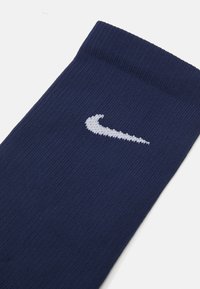 Ciorap ribbed de culoare bleumarin, fabricat dintr-un material moale, având un logo Nike swoosh alb brodat aproape de vârf.