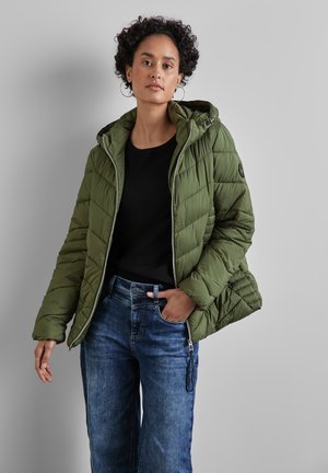 Quilted olive green puffer jacket with a hood, zip closure, and elastic cuffs, paired with dark blue denim jeans and a black shirt.