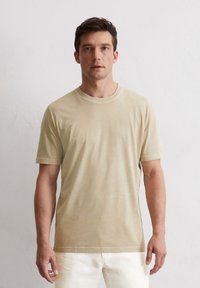 Hellbeige T-Shirt mit kurzen Ärmeln aus weichem Stoff, mit rundem Halsausschnitt und sauber genähten Säumen, kombiniert mit weißen Hosen.