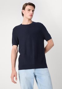Maglioncino a maniche corte di colore blu navy, con colletto rotondo, tessuto strutturato e taglio dritto, abbinato a jeans blu chiaro.
