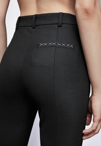 Zwarte op maat gemaakte broek met een gladde textuur, voorzien van een kruissteekdetail op de achterzak en een aansluitende tailleband.