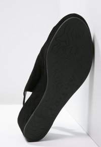 Černá semišová bota s měkkou, strukturovanou černou gumovou podešví. Má mírný podpatek a hladký řemínek přes horní část.