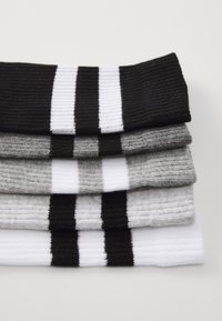 Vier Paar gerippte Socken gestapelt: schwarz mit weißen Streifen, grau, hellgrau und weiß mit schwarzen Streifen. Verschiedene Wollmischungen.