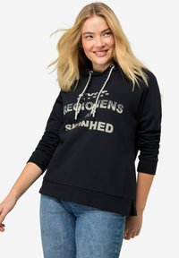 Sudadera negra con capucha, texto impreso en blanco, cordones ajustables, puños acanalados y un ajuste holgado, combinada con jeans de color azul claro.