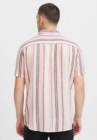 Camisa de manga corta hecha de tela ligera, con rayas verticales en rosa, blanco y colores oscuros. Cuello abotonado y dobladillo curvado.