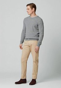 Grijze geribde trui, beige broek en bruine enkellaarsjes. De trui heeft een ronde halslijn en de broek heeft een rechte pijp.